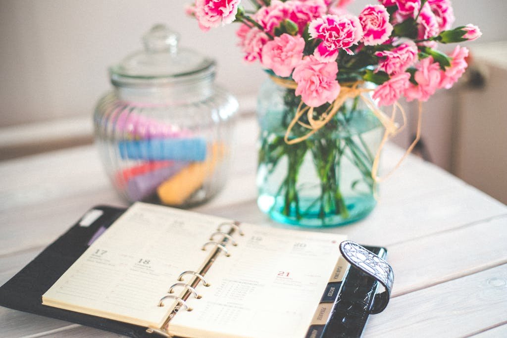 A chic desk setup with an open planner and a vase of pink flowers, ideal for productivity.